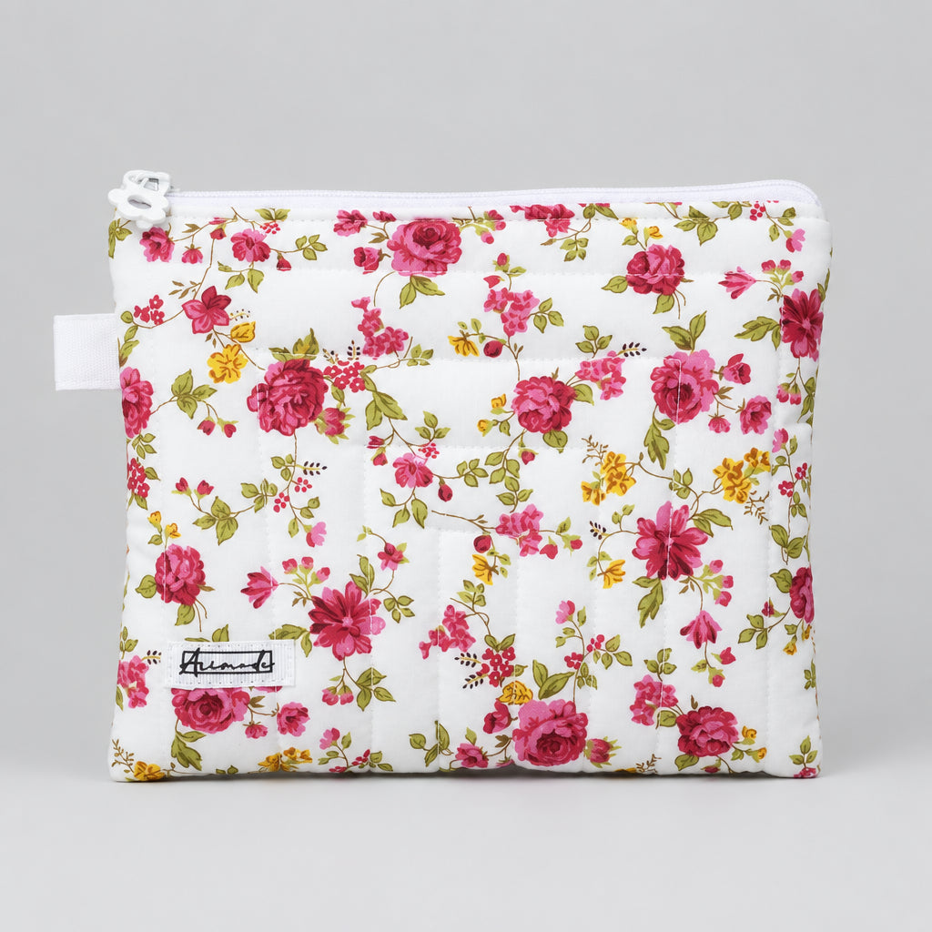 A quilted cosmetic pouch with a white background and an all-over pink, red, and yellow floral print, featuring a white zipper.
